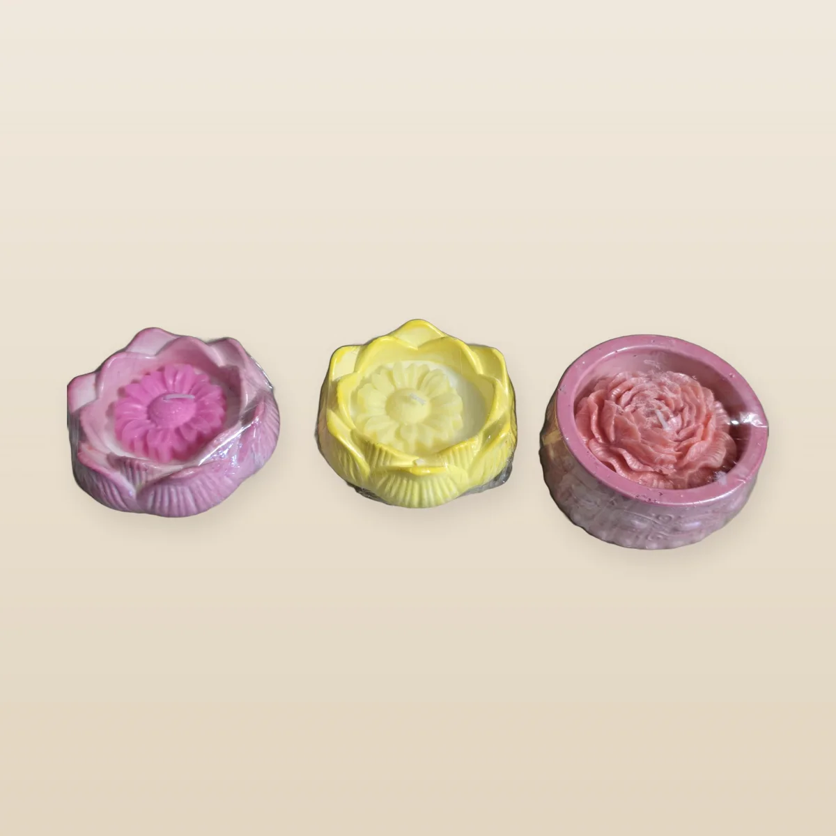 Tre lotusformade vaxobjekt i rosa, gult och rosé